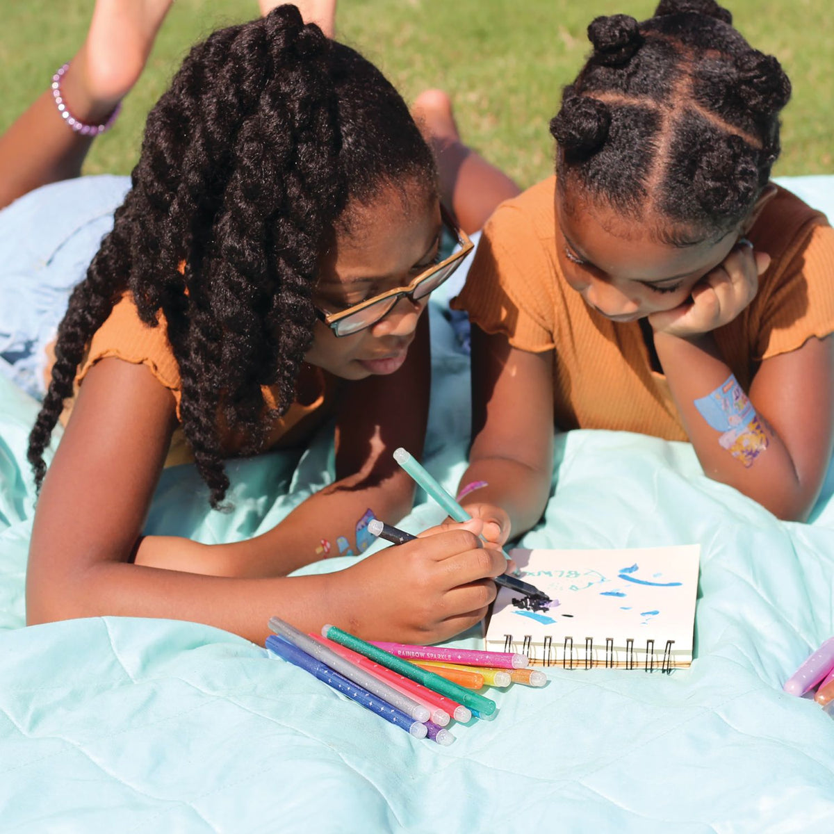 two girls drawing with rainbow sparkle glitter markers in various colors