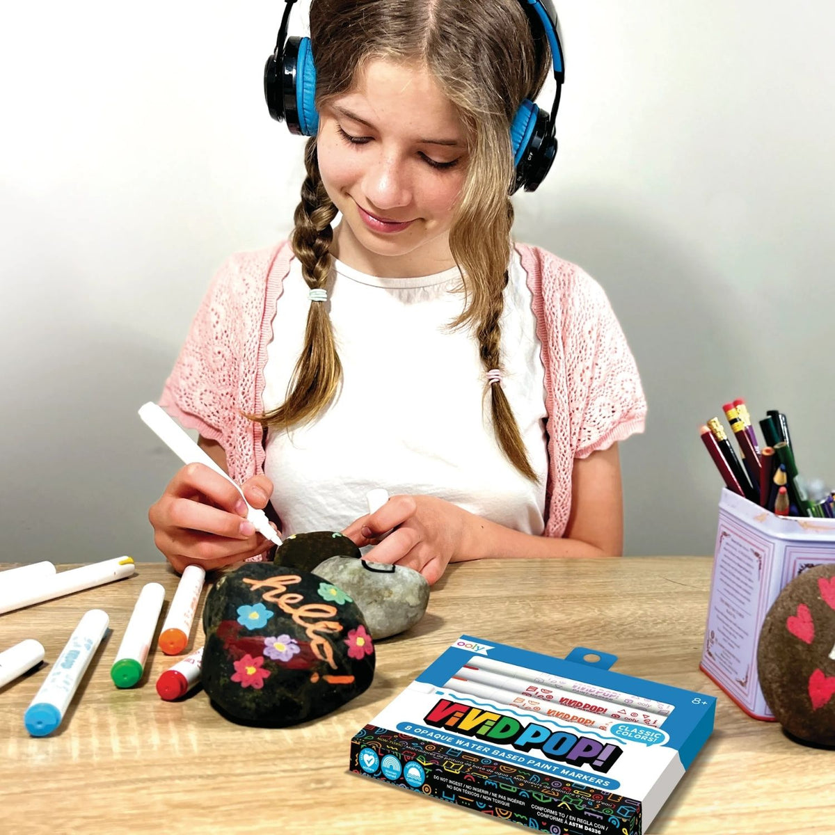 a girl drawing on rocks with Vivid Pop! Water Based Paint Markers Metallic, displaying 8 markers with metallic colors.