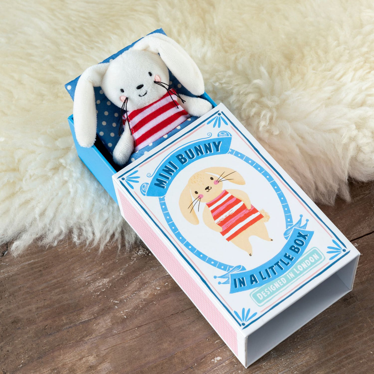 Mini bunny plush toy in a decorative box on a wooden surface with a fluffy white background