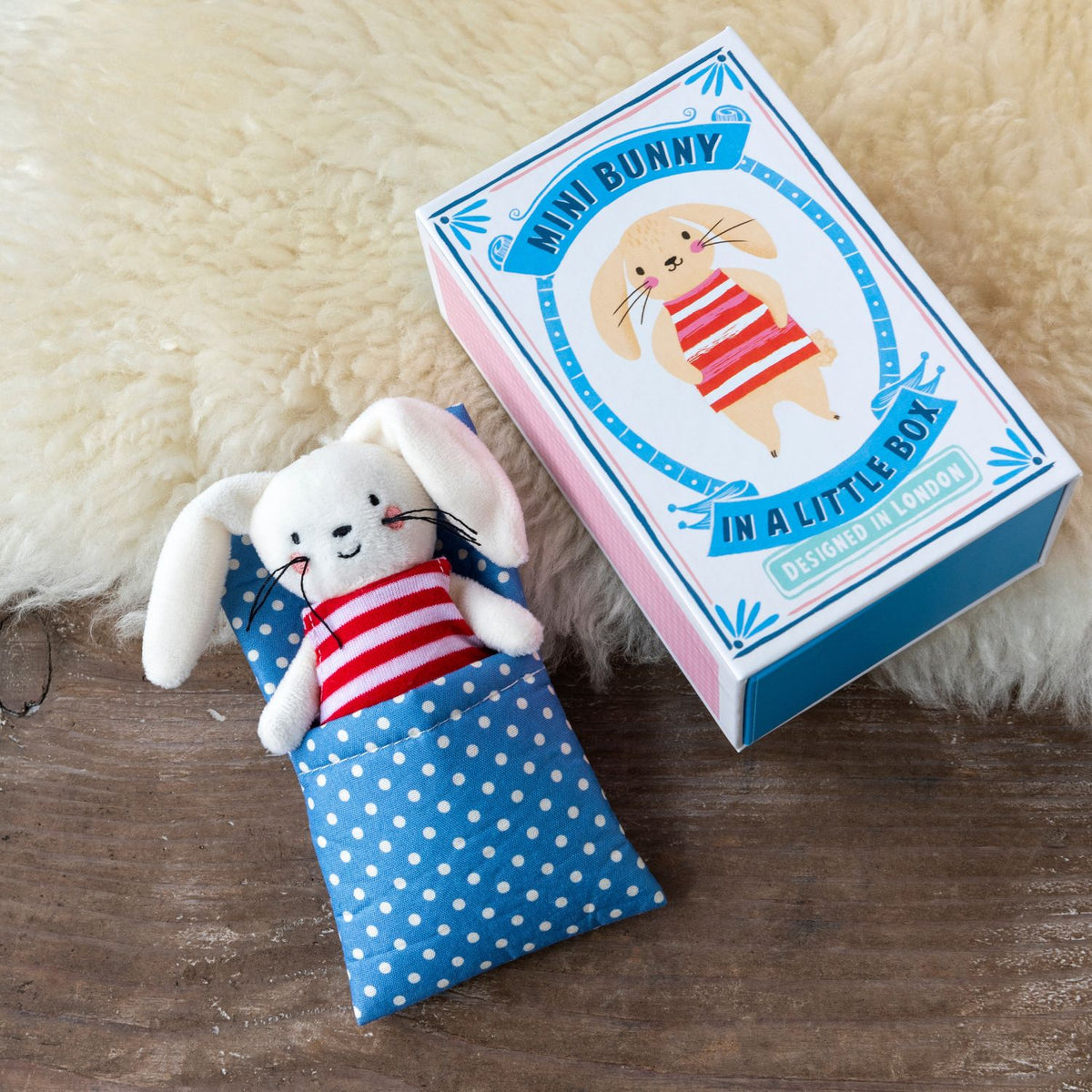 Mini bunny plush toy in a blue polka dot bag next to its packaging on a wooden surface.
