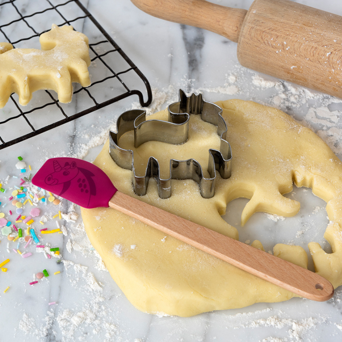Cookie dough with animal-shaped cutters and a spatula on a marble surface.
