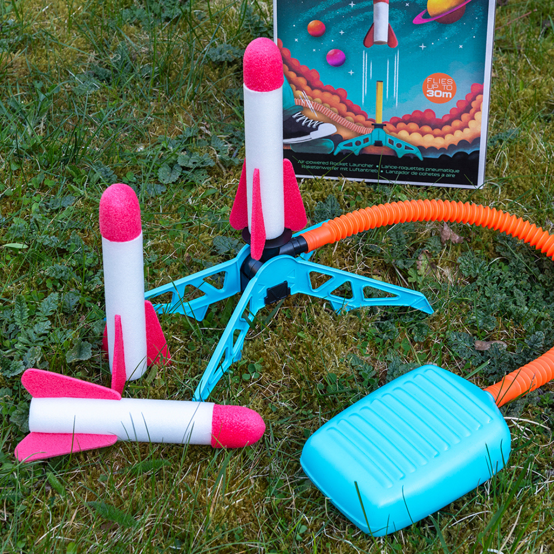 Colorful toy rocket launcher set on grass with a colorful box in the background.