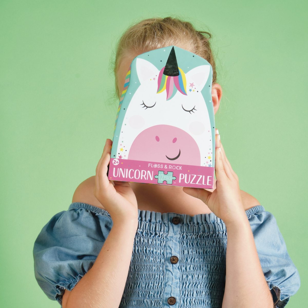 A little girl holding the packaged 12 piece shaped puzzle depicting a colorful unicorn