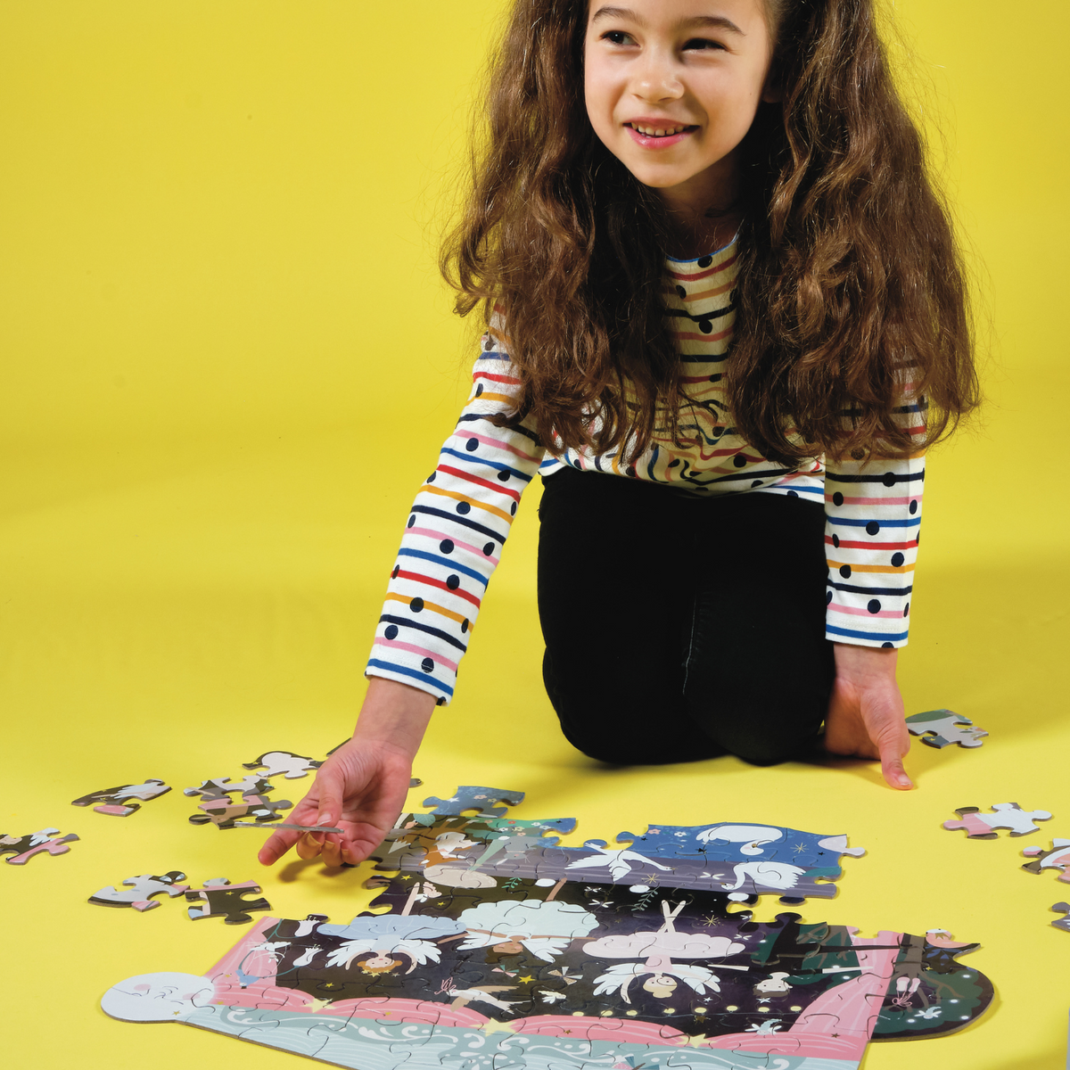 a girl building the fairy tale theme puzzle featuring ballet dancers and forest animals, with a shiny foiled finish.