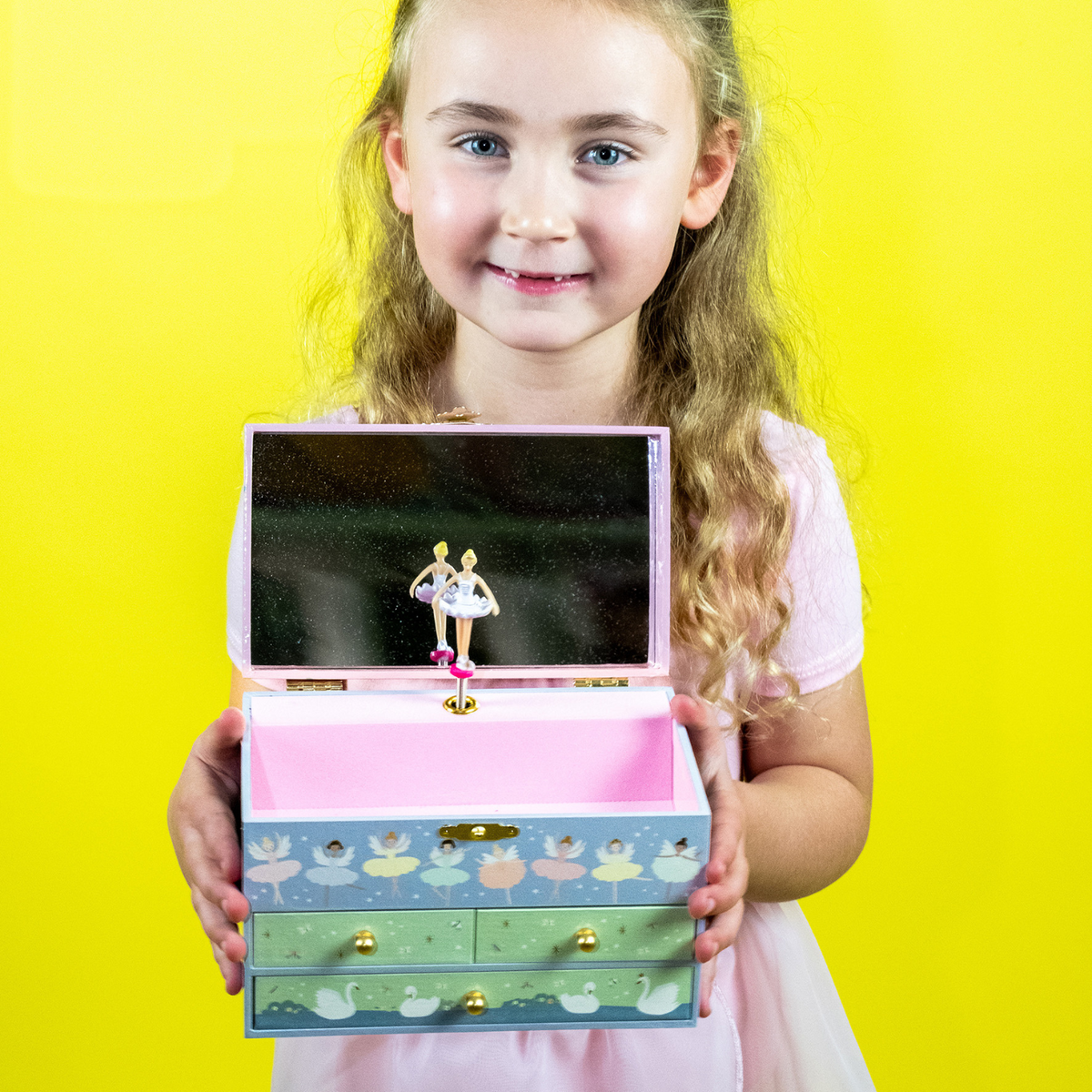 a girl holding A musical jewellery box with 3 drawers, illustrated with ballerinas and swans, packaged in a box.