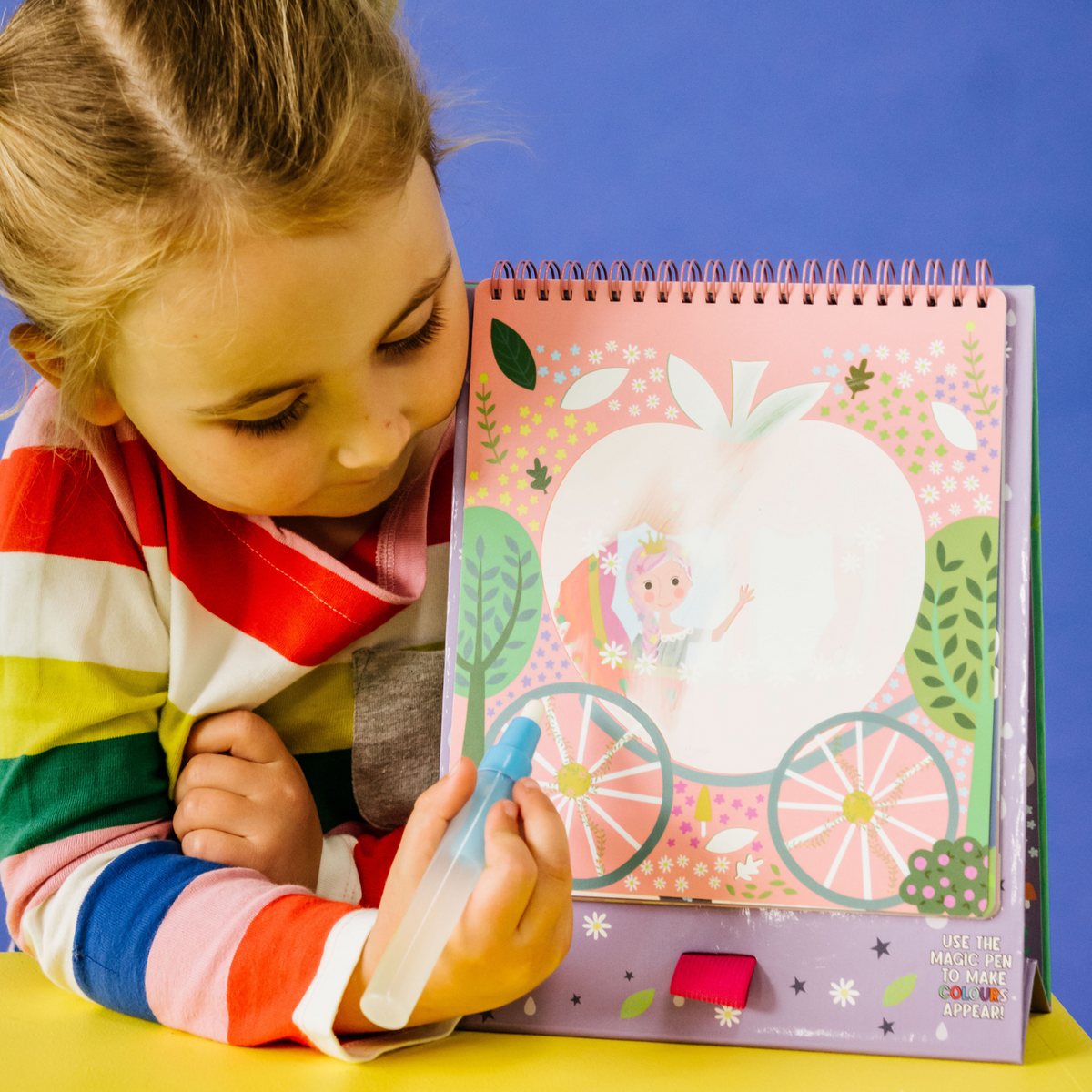 a girl drawing on the magic water color changing easel and pen with illustrations of animals and a fairy on the cover, along with a blue water pen.