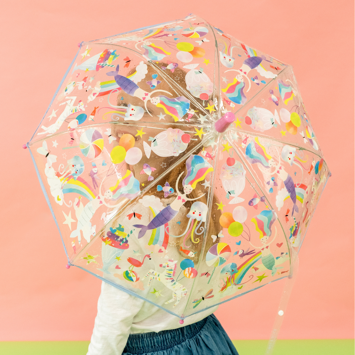 a girl holding A transparent children&#39;s umbrella with colorful animal and fantasy character illustrations, featuring a rainbow, mermaids, and other elements.
