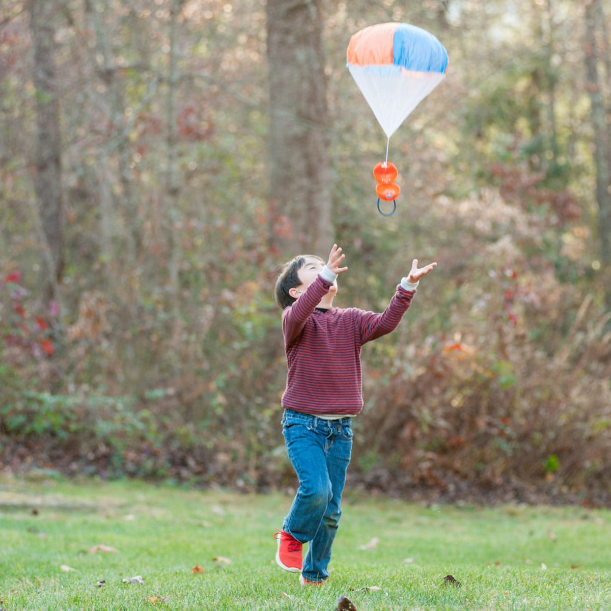 A kid running across a green lawn, laughing as they track the parachute's descent to the ground.