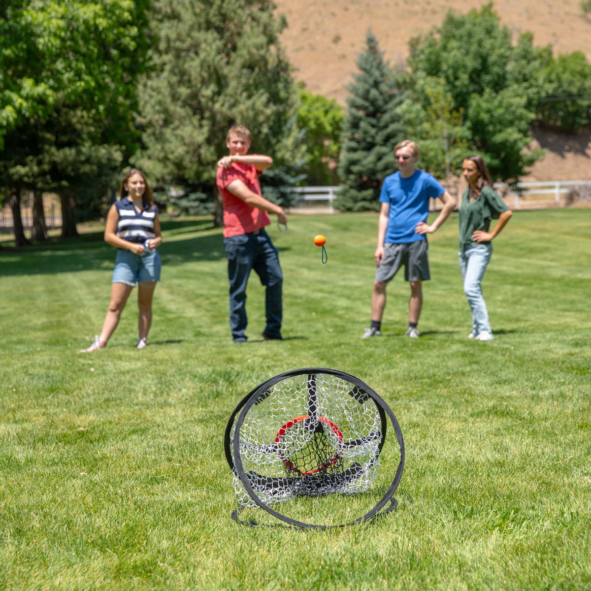 Teenagers standing side-by-side on a green lawn, taking turns launching balls at the target net positioned across the yard.