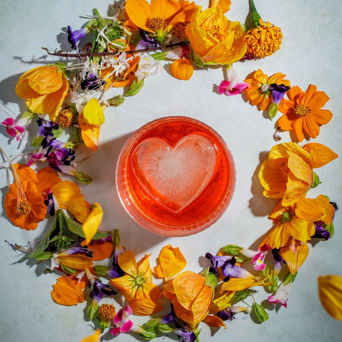 A large, clear ice heart from a heart shaped ice mould floating in a vibrant orange cocktail, illustrating its slow-melting and romantic appeal.
