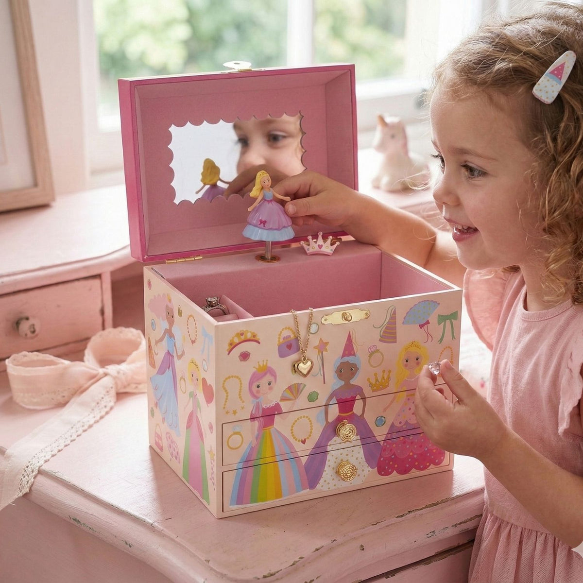 Child playing with the shimmering princess jewellery box sitting on a pink dresser, reflecting light off the metallic foil accents in a brightly decorated child's bedroom.