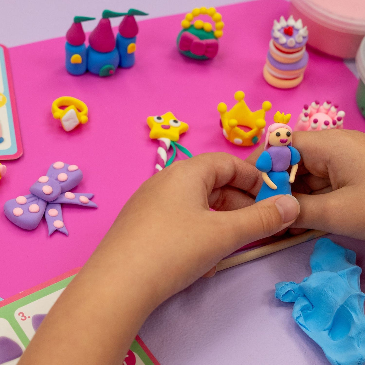 A child's hands with the ultimate kids' clay sculpting kit for princess lovers. Create crowns, castles, and more with 10 colours of soft clay and a wooden stylus. A great screen-free gift!