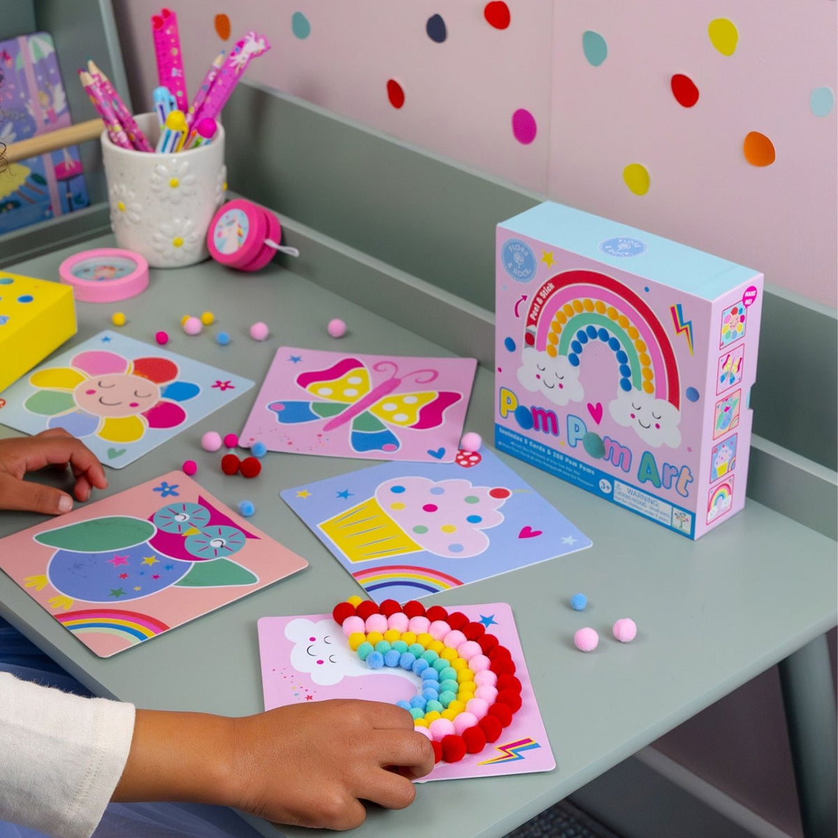 A finished pom pom art piece of a colourful rainbow and sun sitting on a child's bedside table, showcasing the tactile texture and vibrant colours.