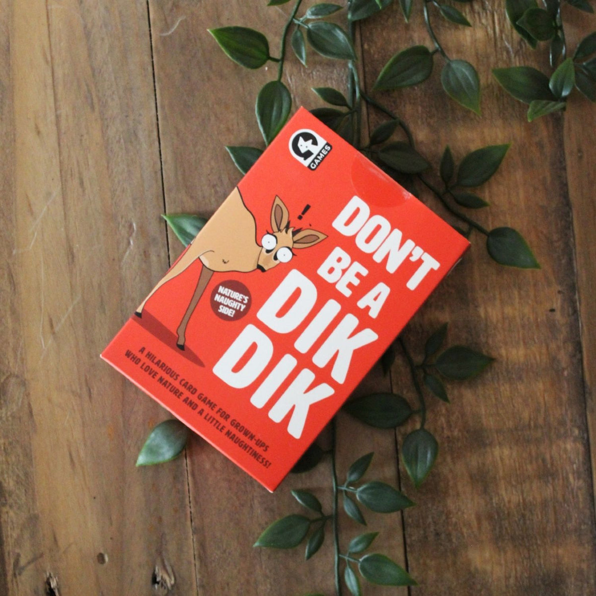 Red game box with 'Don't Be a Dik Dik' text on a wooden surface with leaves.