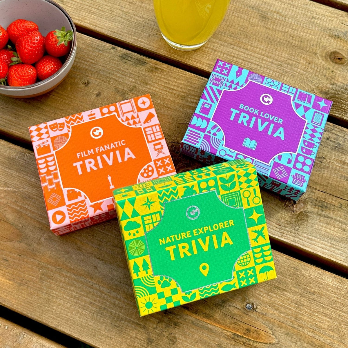 Three colourful trivia boxes with Nature Explorer trivia on the top on a wooden surface with strawberries and juice.