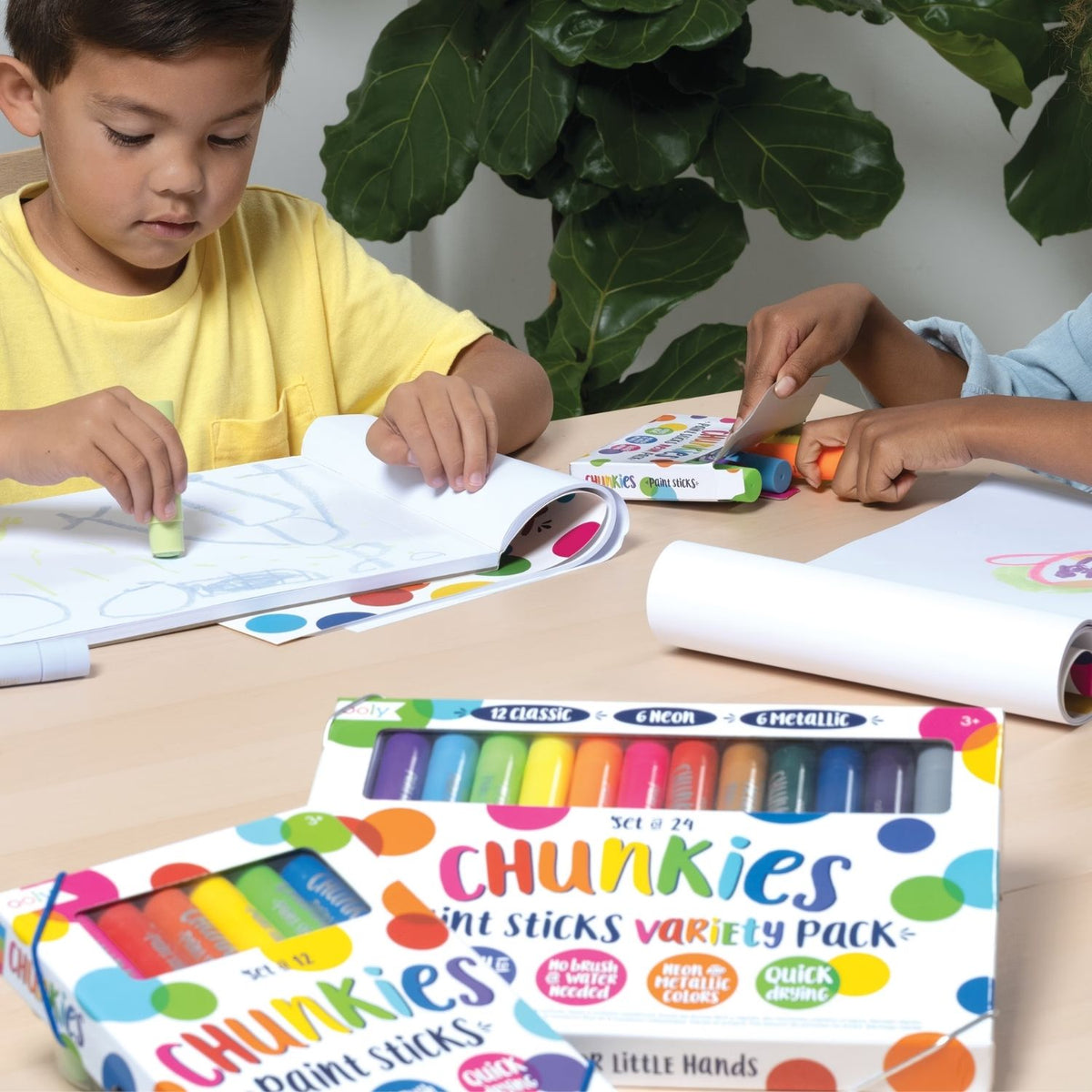Child colouring with Chunkies paint sticks on a table with a plant in the background