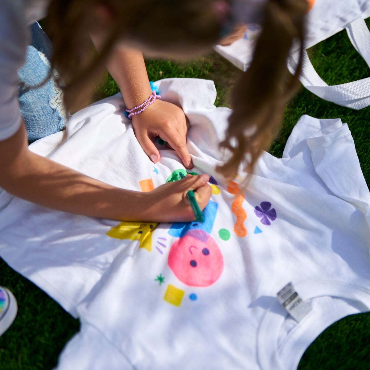 Children's hands coloring on a white blanket with colorful markers outdoors.