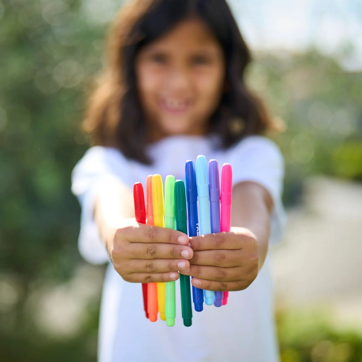 Child holding colorful markers with a blurred natural background