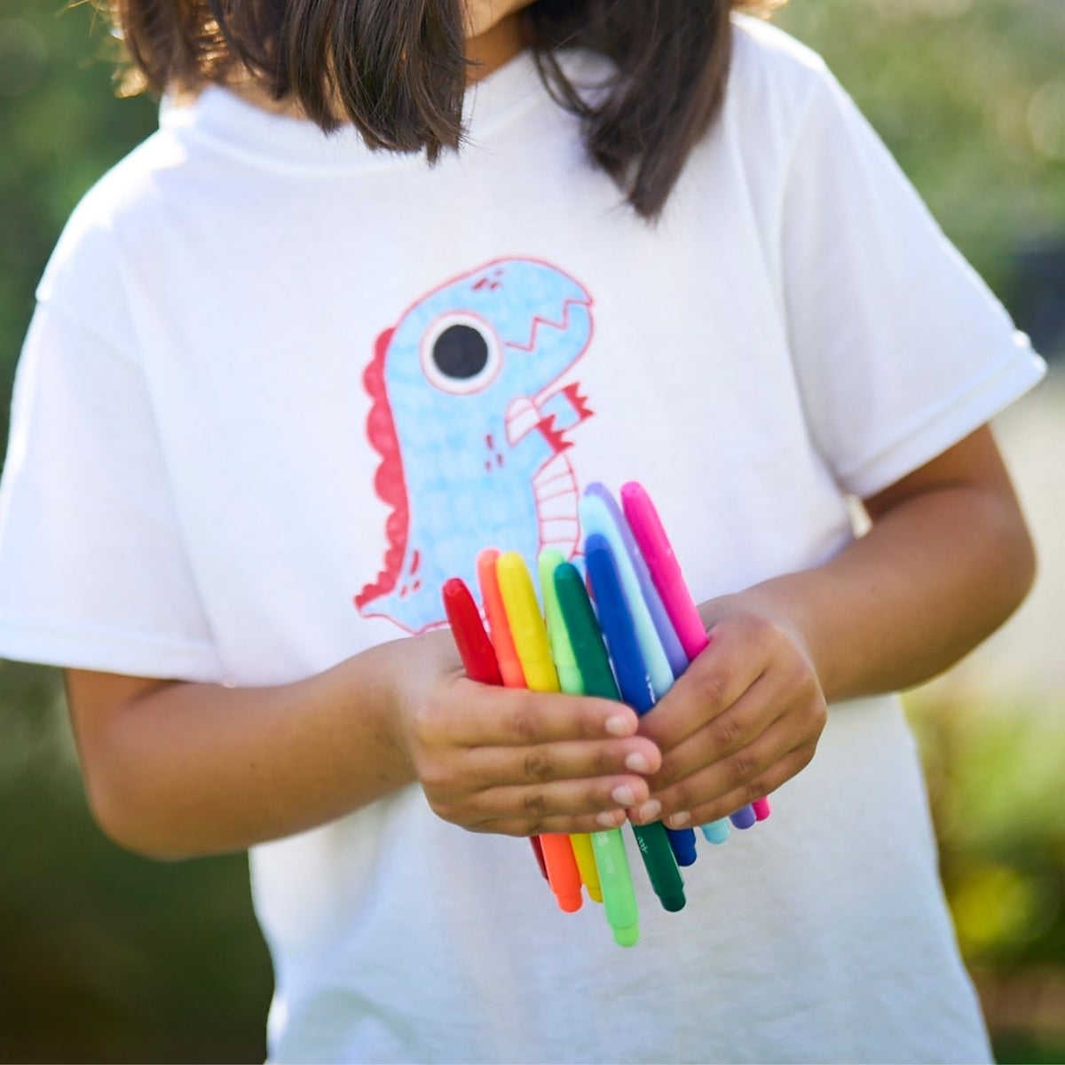 Person wearing a white t-shirt with a colorful dinosaur design, holding rainbow-colored markers.