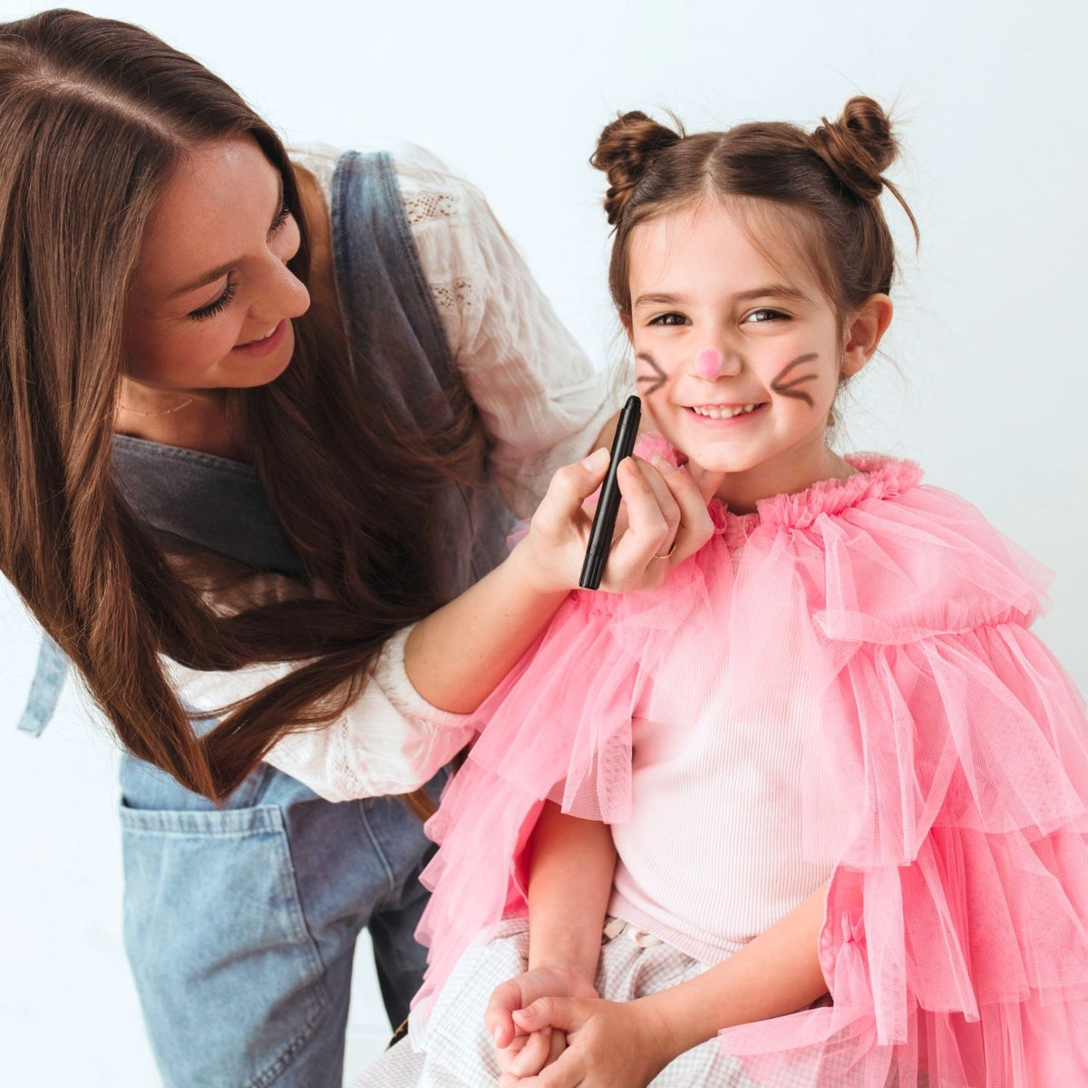 Woman drawing on a child's face with body doodlers, both smiling against a white background