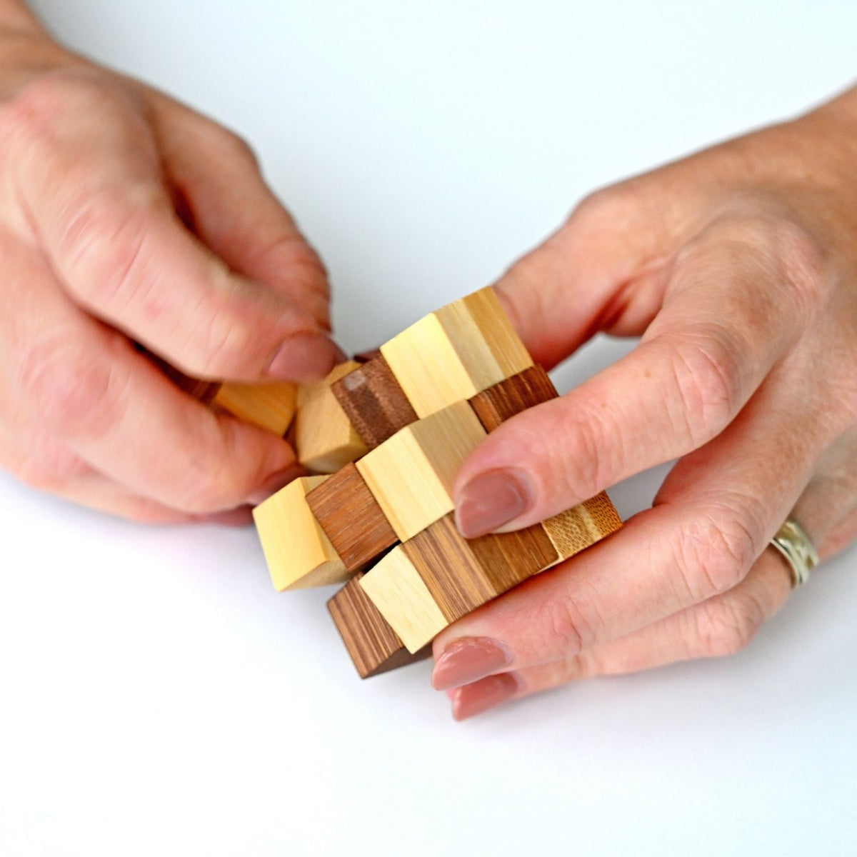 A person’s hands attempting to solve one of the bamboo puzzles from the six-pack, demonstrating the tactile and portable nature of the game.