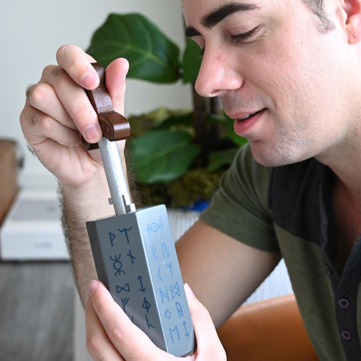 A person’s hands twisting and turning the metal sword hilt to navigate the internal mechanism and release the blade from the wooden stone.