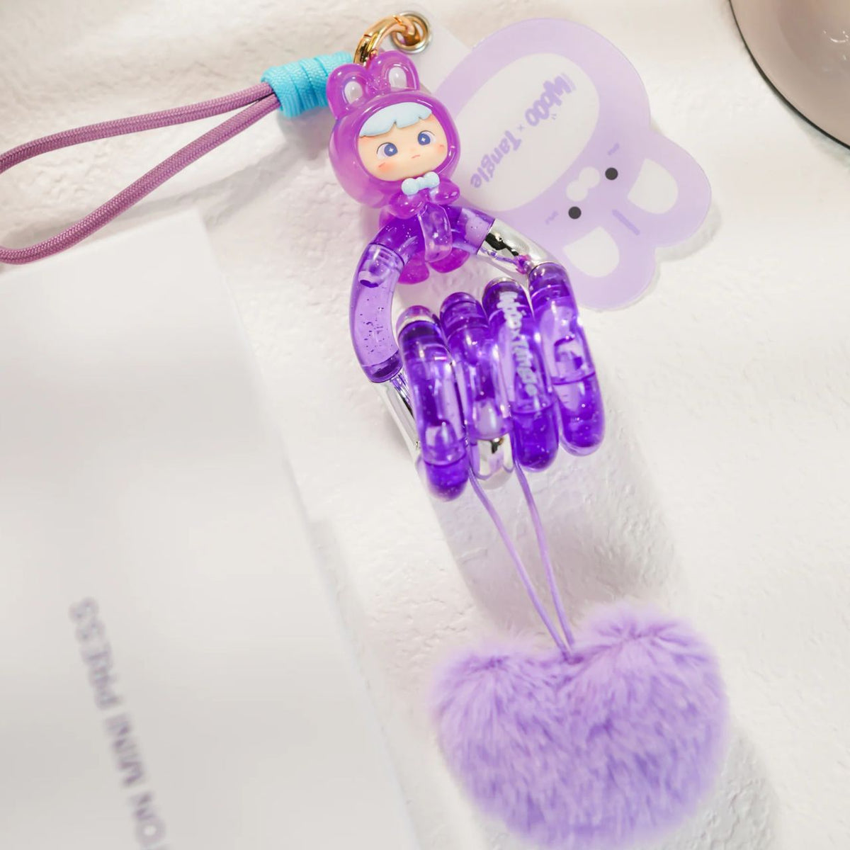 A close-up product shot on a clean white background focusing on the Purple sensory Tangle, twisted into a continuous loop to highlight its smooth, uniform lilac plastic segments and pom pom.